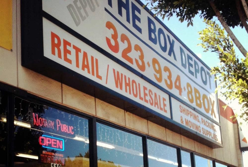 Storefront of The Box Depot with large signage for retail, wholesale, and notary public services.