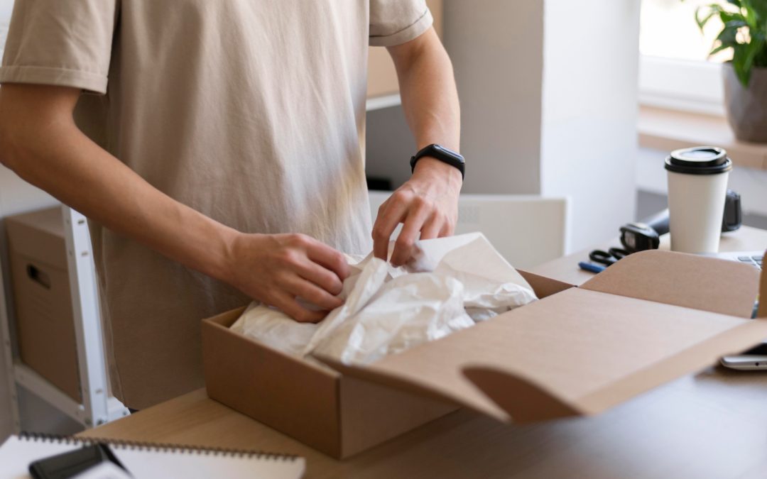 Person opening a cardboard box with tissue paper inside at a desk with a coffee cup and notebook nearby.