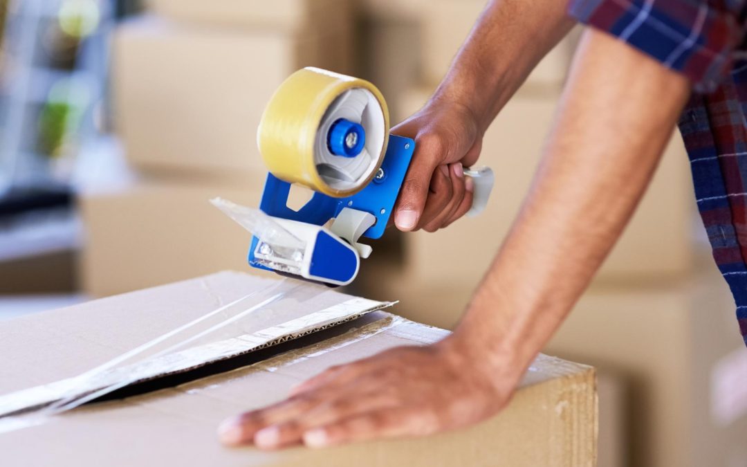 Close-up of a person sealing a cardboard box with packing tape and a tape dispenser.