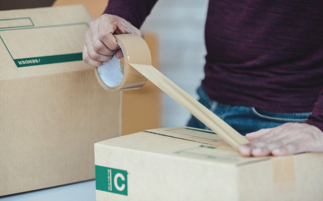 A person sealing a cardboard box with packing tape next to another box.
